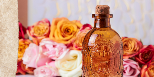 Der berühmteste Attar ist Attar of Roses: Hellbraune verzierte Flasche vor einem Hintergrund voller Rosenblüten.